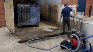 Technician capturing wastewater from dumpster pad
