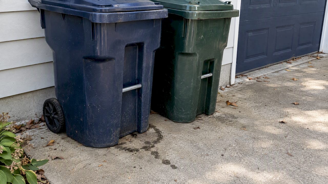 Leaking trash bins beside a stained concrete pad